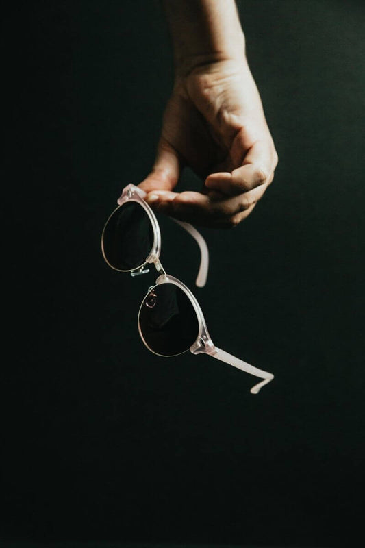 Hand holding stylish round pink sunglasses against a dark background.