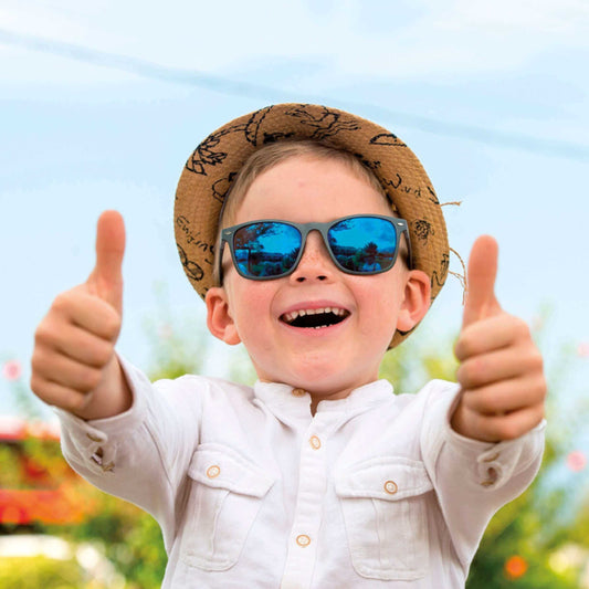 Happy child wearing stylish sunglasses and a hat giving thumbs up in a sunny outdoor setting.