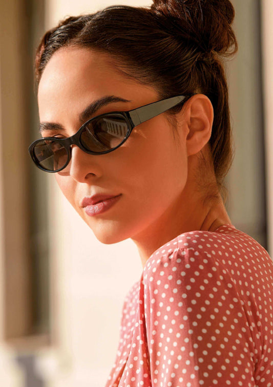 Stylish woman wearing sleek black sunglasses and a polka dot top, highlighting modern eyewear fashion.